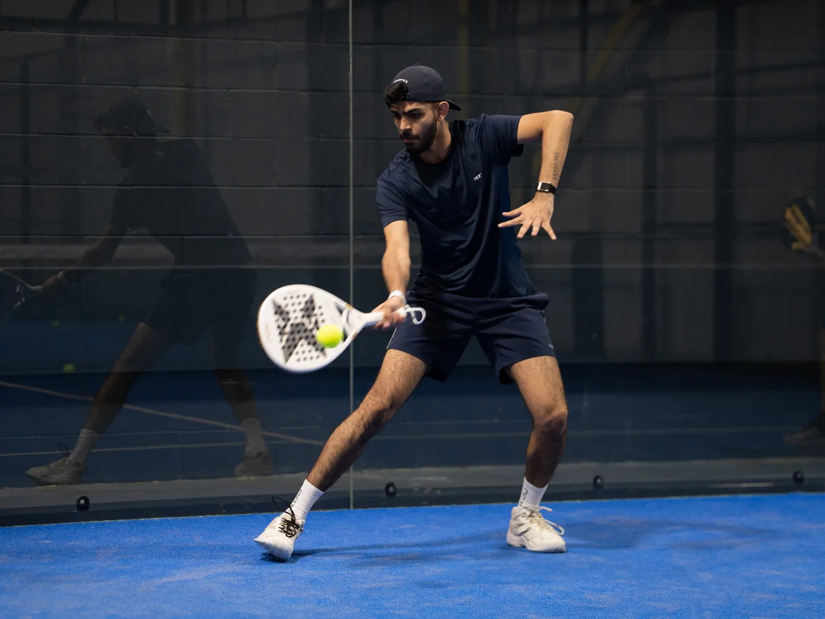 A player bends low to hit a forehand beside the glass.