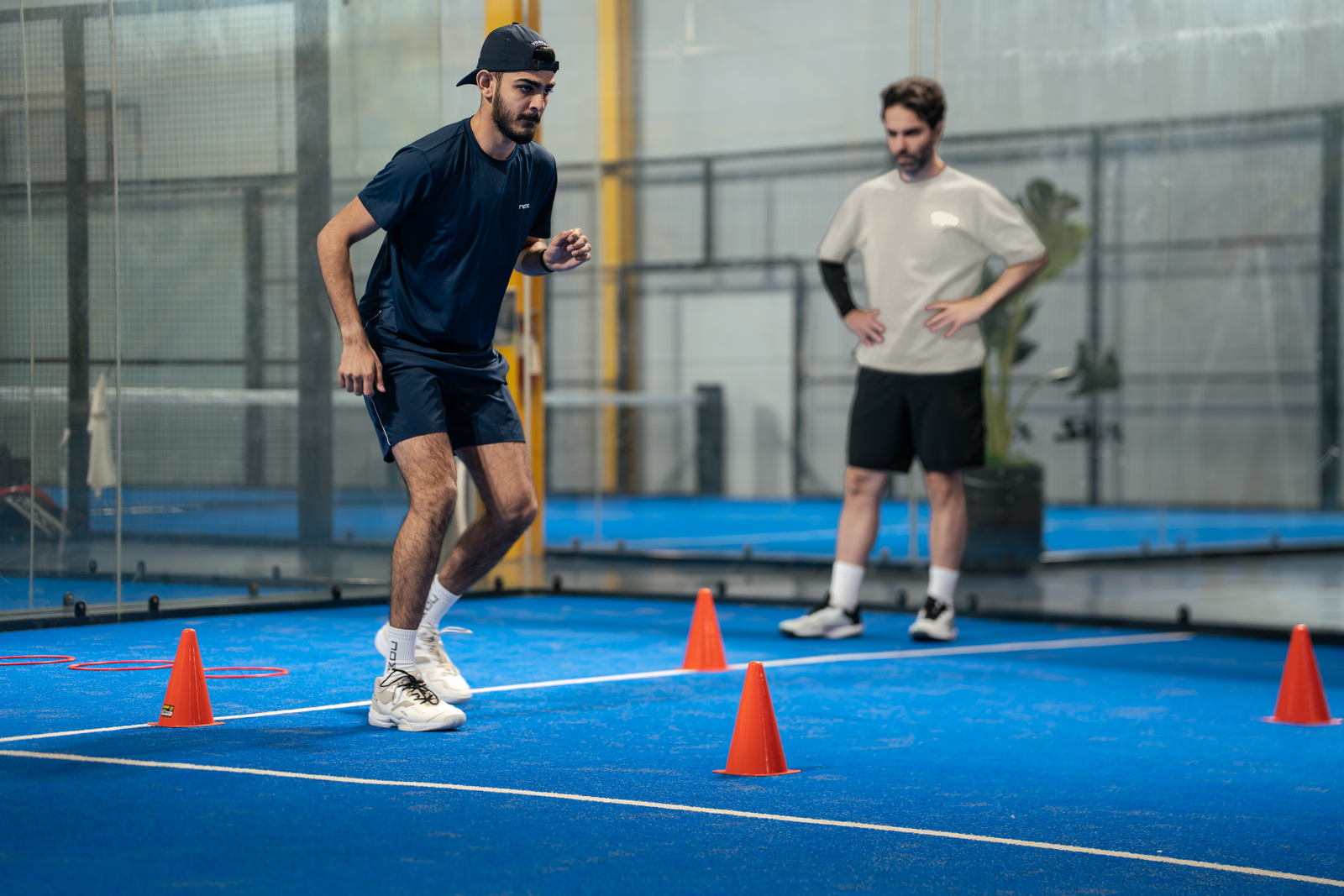 A player runs through cones on court while a coach watches.