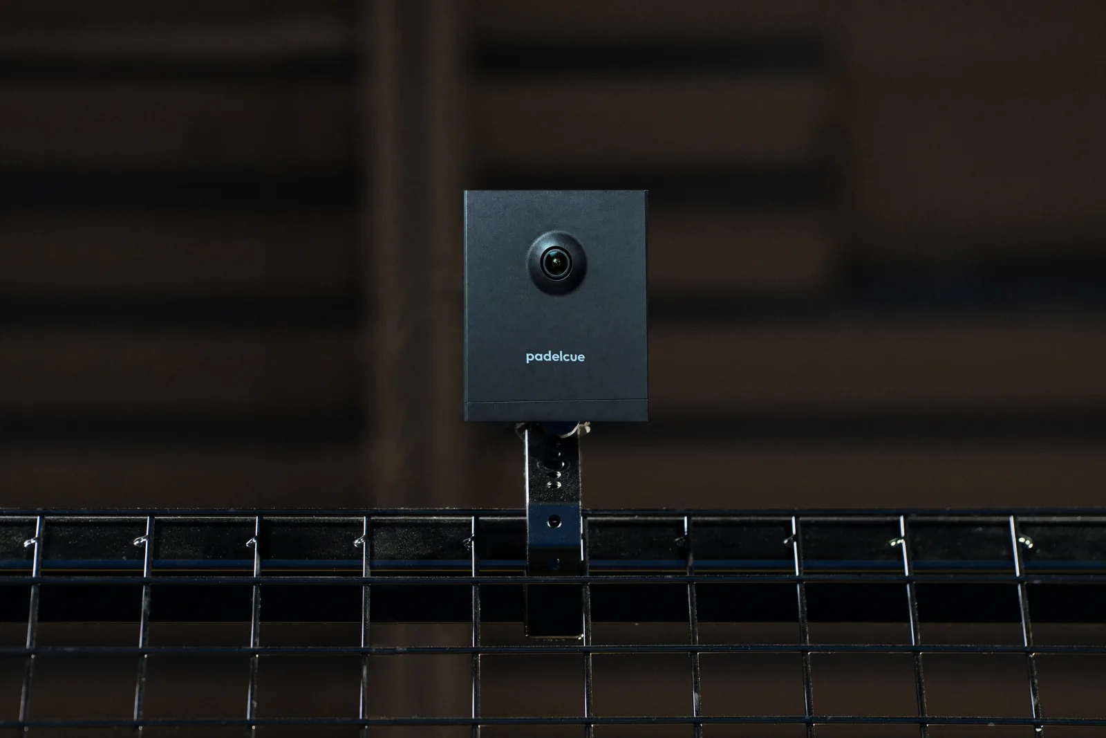 Composite image of the PadelCue court camera on the top rail of a court fence, its lens facing the court.